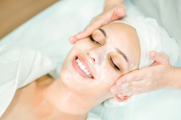 Fototapeta na wymiar Beautician makes facial massage with mask. Beautiful smiling girl on spa procedure by face.