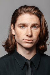 Portrait of a man with long hair and freckles, dressed in a black shirt and black tie