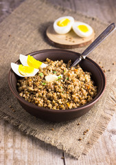 Buckwheat porridge with mushrooms on a plate. Buckwheat porridge in black casserole on wooden background closeup