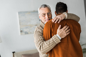 happy senior man in glasses smiling while hugging son