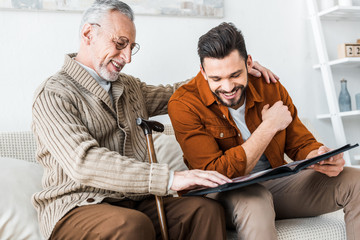 handsome man smiling while holding photo album near senior dad