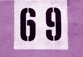 Number 69 on cement wall in stencil in purple tone.