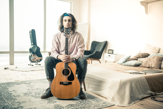 Long-haired young musician resting in stylish bedroom