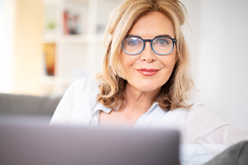 Frau mit Brille zuhause auf der Couch mit laptop 