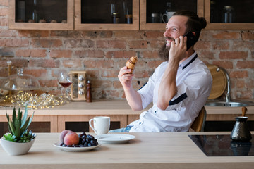 Hipster morning. Fruit and pastry snack for breakfast. Cup of drink. Good news on phone. Excited man talking on mobile.