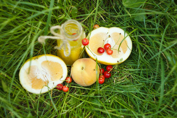 a bottle of homemade lemonade juice with cherry and citrus fruits lies on the grass outdoors. Picnic on nature in the park against the backdrop of trees with bright sunshine. healthy food, diet