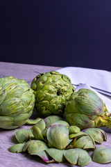 Obraz premium Artichokes On Gray Wooden Background, knife and napkin. fresh organic artichoke flower
