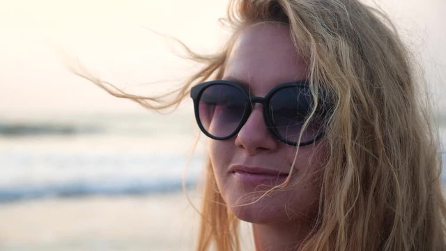 The face of a charming blonde girl with flowing hair against the sea. Portrait of a beautiful young woman smiling at sunset.