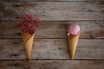creamy raspberry ice cream with raspberry berries and pink flowers in a waffle cone on an old...