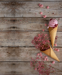 Fototapeta na wymiar creamy raspberry ice cream with raspberry berries and pink flowers in a waffle cone on an old wooden table