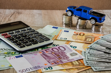 Dollars, euros, coins, a calculator and a toy blue car on a wooden background