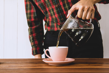 Barista is pouring water, drip coffee into  cup of pink coral on a wooden table.