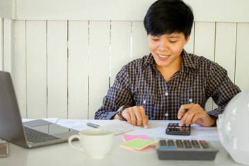 Asian businessman Writing paper and using calculator Calculating bonus(Or other compensation) to employees to increase productivity on desk with hot chocolate. Selective Focus