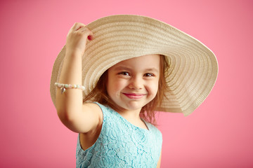 Beautiful little girl in beach hat stands over pink isolated background.