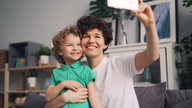 Pretty girl mother is taking selfie with cute son laughing and having fun holding smartphone with camera. Modern technology and family photographs concept.