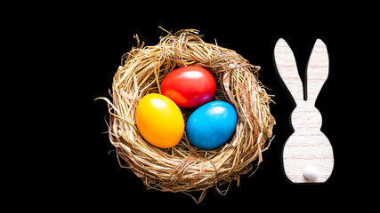 Bunte Eier im Osternest mit Hase vor einem schwarzen Hintergrund