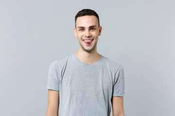 Portrait of cheerful smiling young man in casual clothes showing tongue, looking camera isolated on grey wall background in studio. People sincere emotions, lifestyle concept. Mock up copy space.