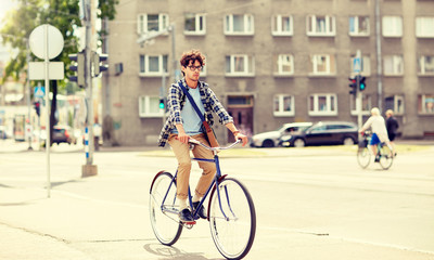 Fototapeta premium people, style, leisure and lifestyle - young hipster man with shoulder bag riding fixed gear bike on city street