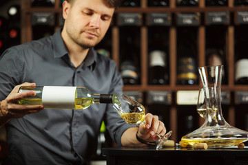 Sommelier pouring white wine from bottle in glass