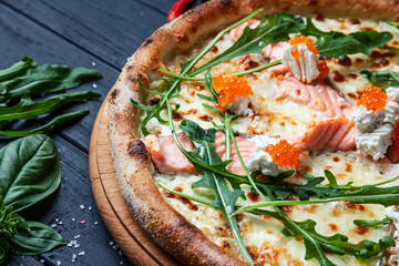 Close up view on pizza with salmon and caviar on dark wooden table. Pizza, cheese, cherry tomato and parsley on dark wooden background with copy space for design. Top view food menu, recipe