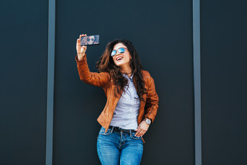 Young modern woman taking selfie leaning against a dark wall