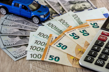 Dollars, euros, a calculator and a toy blue car on a wooden background