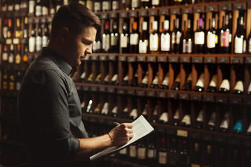 Sommelier writes at notes, putting down information on wine products in cellar