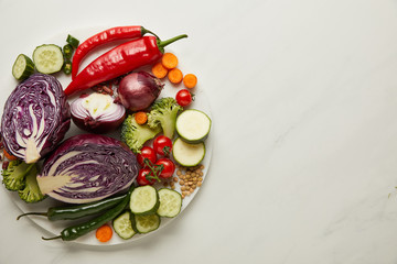 Top view of whole and cut vegetables on white surface