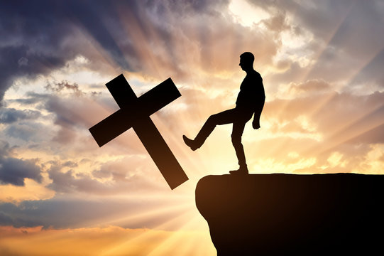 Man atheist pushes the symbol of christian cross into the cliff