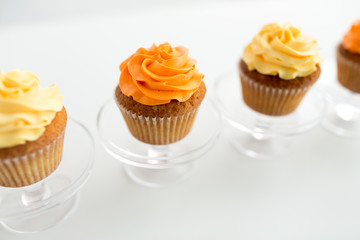 food, pastry and sweets concept - cupcakes with buttercream frosting on glass confectionery stand over white background