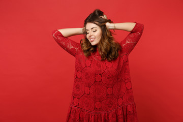 Portrait of charming young woman in lace dress keeping eyes closed, putting hands on head isolated on bright red background in studio. People sincere emotions, lifestyle concept. Mock up copy space.