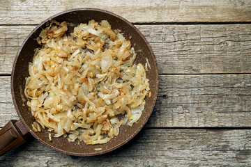 Freshly fried slices of an onion in a stone coated frying pan standing on the wooden boards