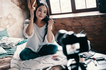 Sharing impressions. Beautiful young woman testing beauty product and smiling while making social...