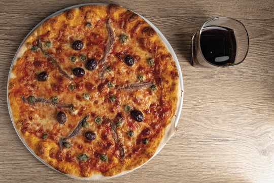 pizza pomodoro acciughe capperi olive nere intera dall'alto nel piatto