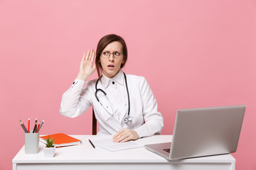 Tired sad female doctor sits at desk work on computer with medical document in hospital isolated on...