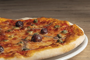 pizza pomodoro acciughe capperi olive nere intera nel piatto da basso primo piano vista destra