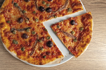 pizza pomodoro acciughe capperi olive nere tagliata dall'alto nel piatto