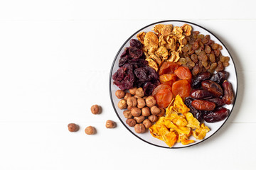 A set of dried fruits (apples,dates,pumpkin,apricot,cherry) and hazelnuts lying on a white plate on a white background.