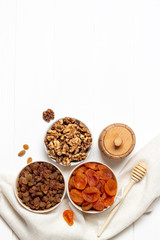 Dried apricots, raisins, walnuts in cups and a barrel of honey standing on a napkin on a white natural background.