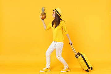 Amazed traveler tourist woman in summer clothes, hat hold fresh ripe pineapple fruit isolated on yellow orange background. Passenger traveling abroad on weekends getaway. Air flight journey concept.