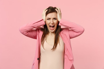 Portrait of screaming frustrated young woman wearing jacket putting hands on head isolated on pastel pink wall background in studio. People sincere emotions, lifestyle concept. Mock up copy space.