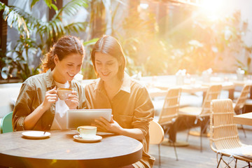 Cheerful beautiful young lady researchers sitting at table and drinking coffee while using modern tablet, they working in greenhouse cafe