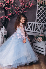Fototapeta premium Cute adorable baby girl in elegant blue wedding dress indoors posing and looking at camera. Childhood, fashion kids concept