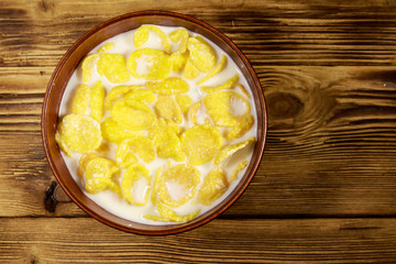 Cornflakes with milk in a bowl on wooden table. Top view