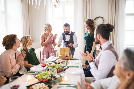 A mature man with friends and family opening presents on a birthday party.