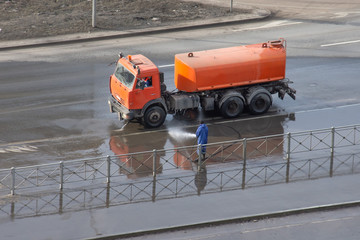 Car with a water tank on the highway, a working man washes a dividing strip asphalt from a hose.