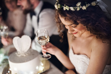 A close-up of a young bride sitting at a table on a wedding, holding a glass of wine.
