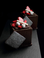 Dark chocolate textured cube dessert with strawberry, silver cookie decorations and red sponge