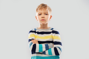 childhood, expressions and people concept - serious little boy in striped pullover with crossed arms over grey background