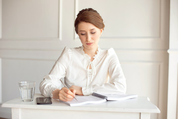 Young woman signs important documents while sitting at her desk in an office. Pretty Caucasian female working in a home office.